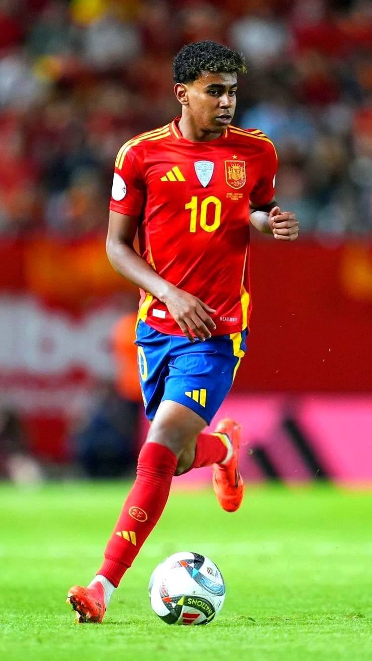 A male soccer player in a red and yellow Spain jersey with the number 10 dribbles a ball on the field during a match, captured in vivid detail as seen on Nordic IPTV. The background is blurred, showing a crowd and stadium lights.
