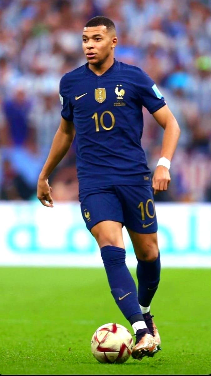 A soccer player in a dark blue France jersey with number 10 dribbles a ball on a field during a match, as seen on Nordic IPTV. The background is blurred, showing a crowd of spectators.