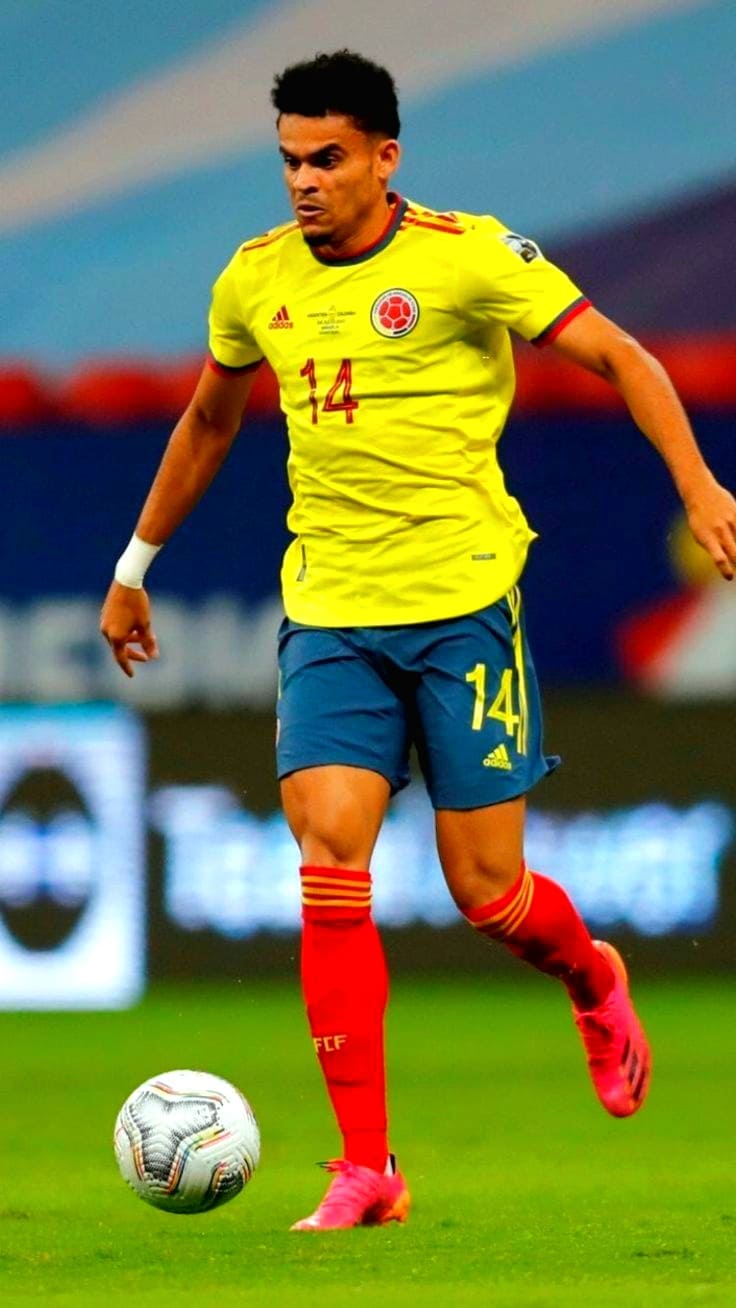 A soccer player wearing a yellow Colombia jersey with number 14, blue shorts, and red socks is running on the field with a ball, while the match is broadcast live via Nordic IPTV.